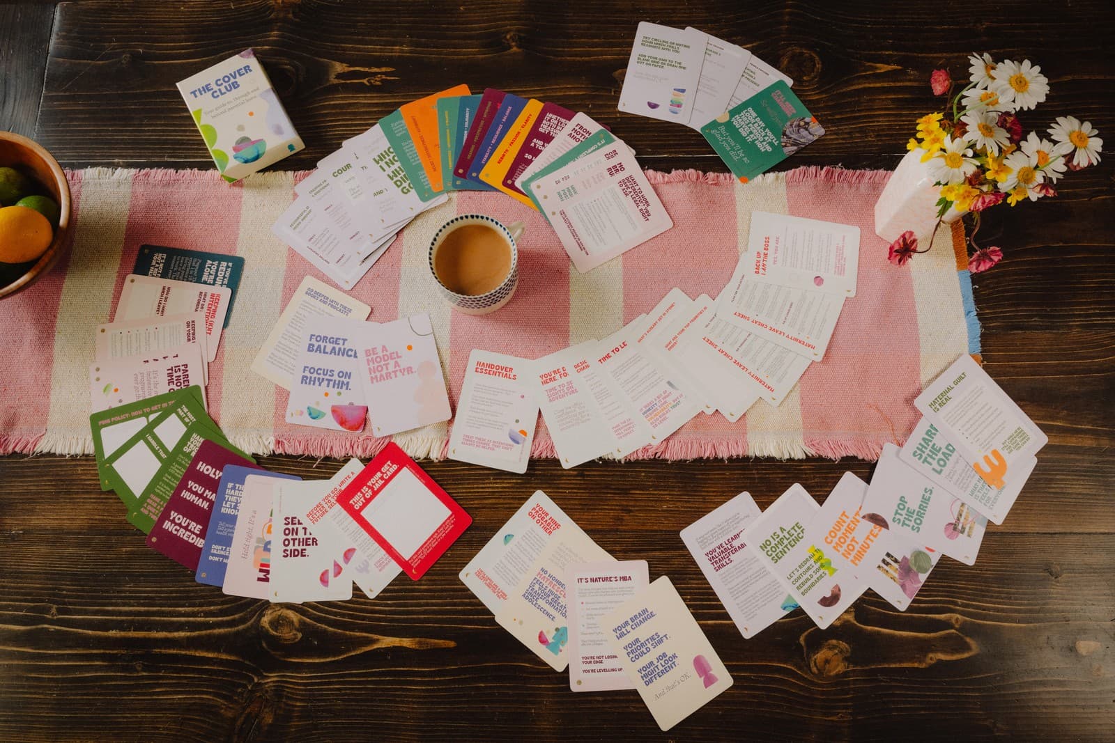 The full set of Cover Club cards spread out on a table with coffee and flowers